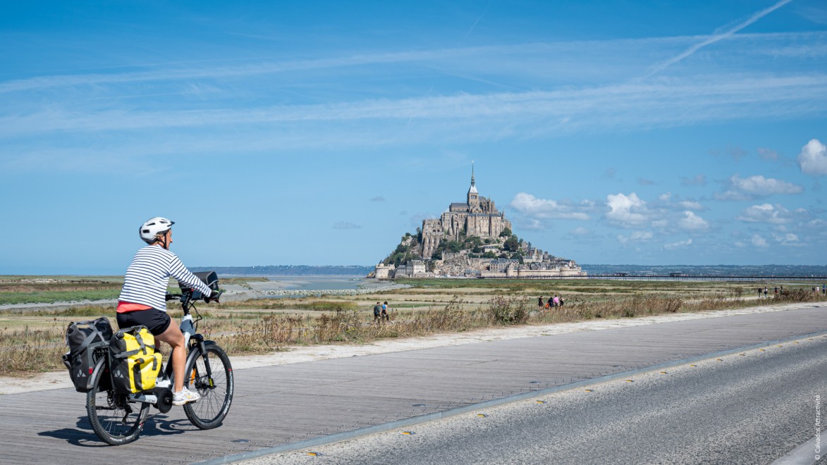 Radfahrer auf einer Strasse vor der beeindruckenden Kulisse des Mont Saint Michel