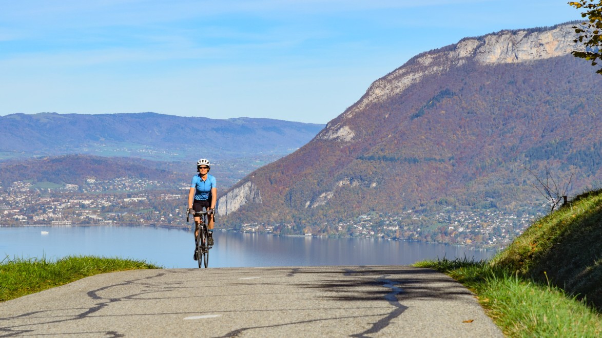 Eine Rennradfahrerin fährt eine kleine Straße hinauf, die den See von Annecy überragt.