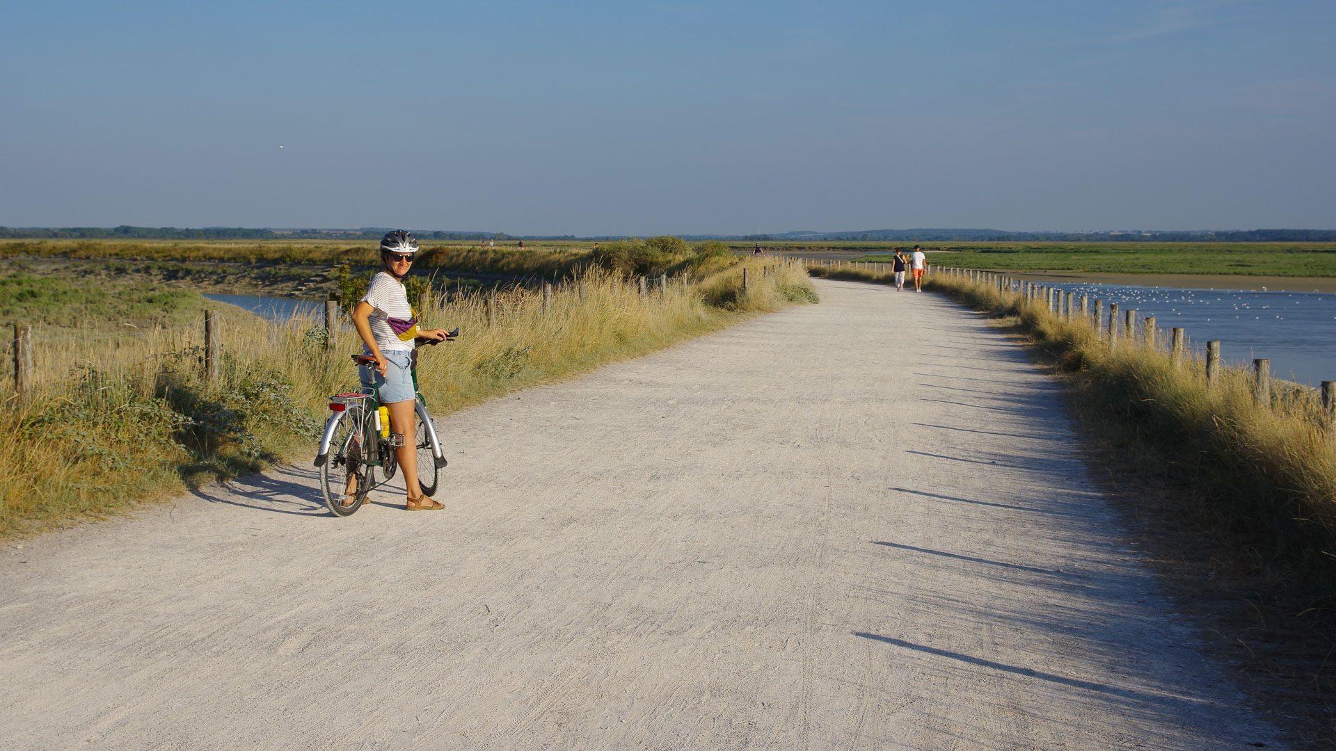 Eine Radfahrerin posiert vor den Salzwiesen der Sommebucht auf einem Weg über den Deich.