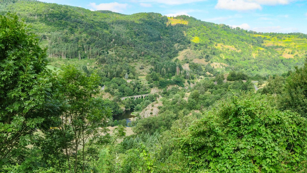 Ausblick auf die wilde Allier-Schlucht mit seinen Felsen und einem Viadukt der historischen Bahnlinie.