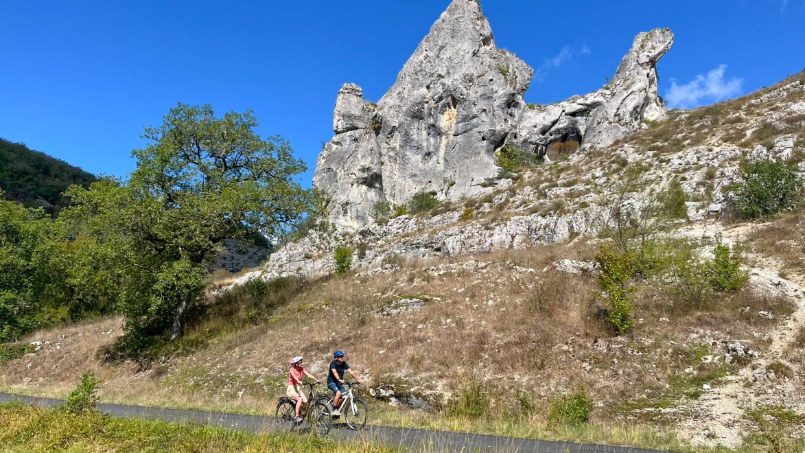 Ein Radfahrerpaar auf einer kleinen Straße, gesäumt von Felsmonolithen, im Naturpark Causses du Quercy