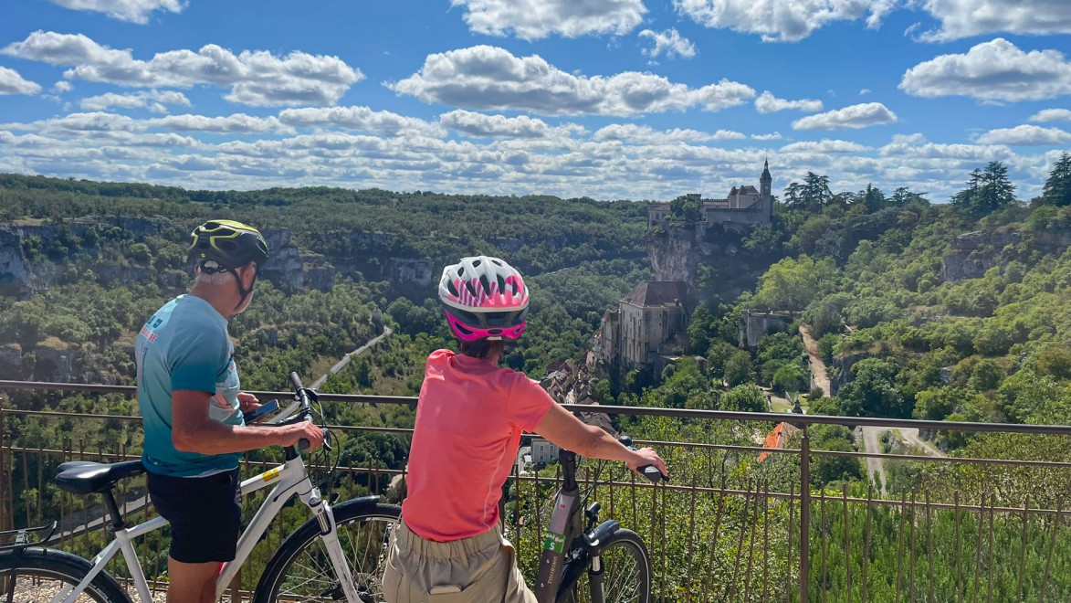 Ein Radfahrerpaar bewundert das hochgelegene Dorf Saint-Cirq-Lapopie im Departement Lot