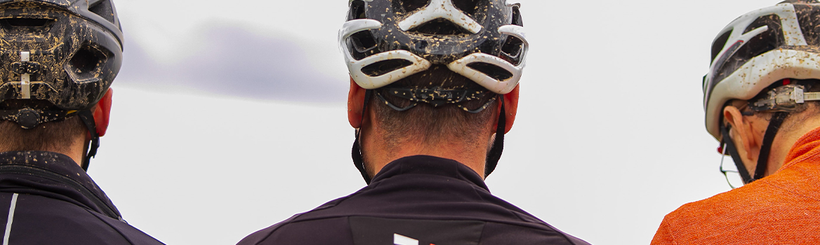 Drei Gravel-Radfahrer von hinten, ihre Helme sind mit Schlamm bespritzt.